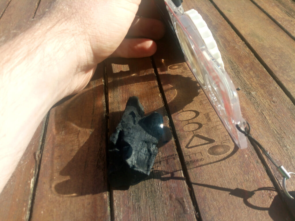 Gebündelte Sonnenstrahlen mit der kleinen Lupe auf ein Stück Kohle gerichtet.