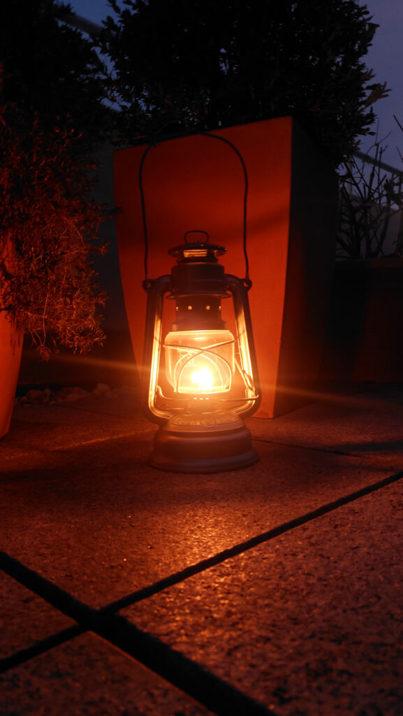 Leuchtende Petroleumlamp von Feuerhand auf der Terrasse im Dunklen