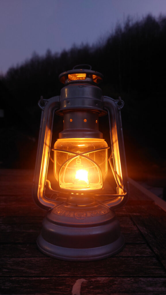 Petroleumlampen Baby Special 276 von Feuerhand. Hier im Dunklen auf dem Gartentisch mit Wald im Hintergrund