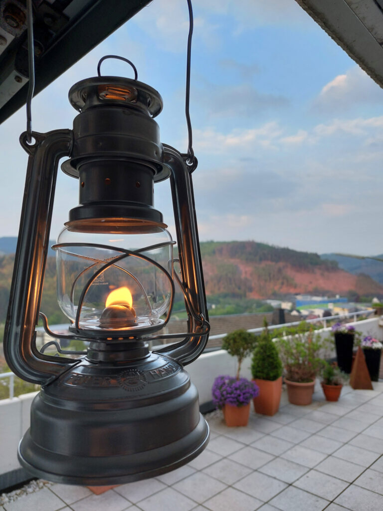 Petroleumlampe Baby Special 276 von Feuerhand im Hellen auf dem Terrasse mit Wald im Hintergrund