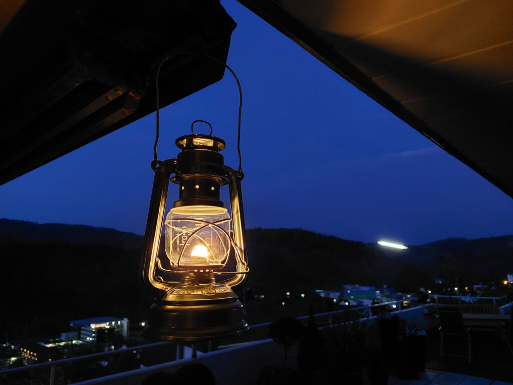Petroleumlampe Baby Special 276 von Feuerhand im Dunklen auf dem Terrasse mit Wald im Hintergrund