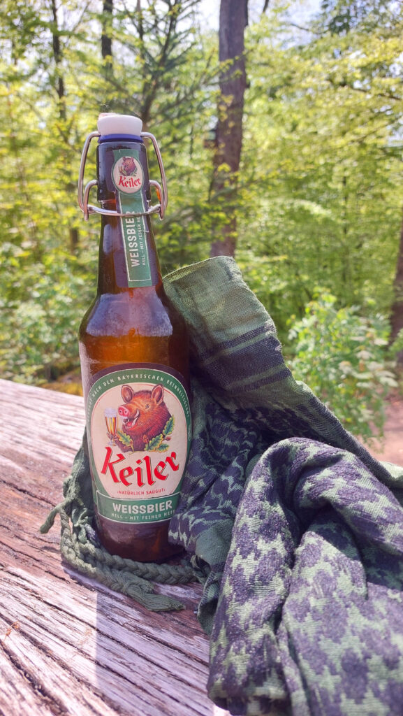 Eine Flasche Keiler Weissbier zusammen mit einem Shemagh auf einem Tisch im Wald